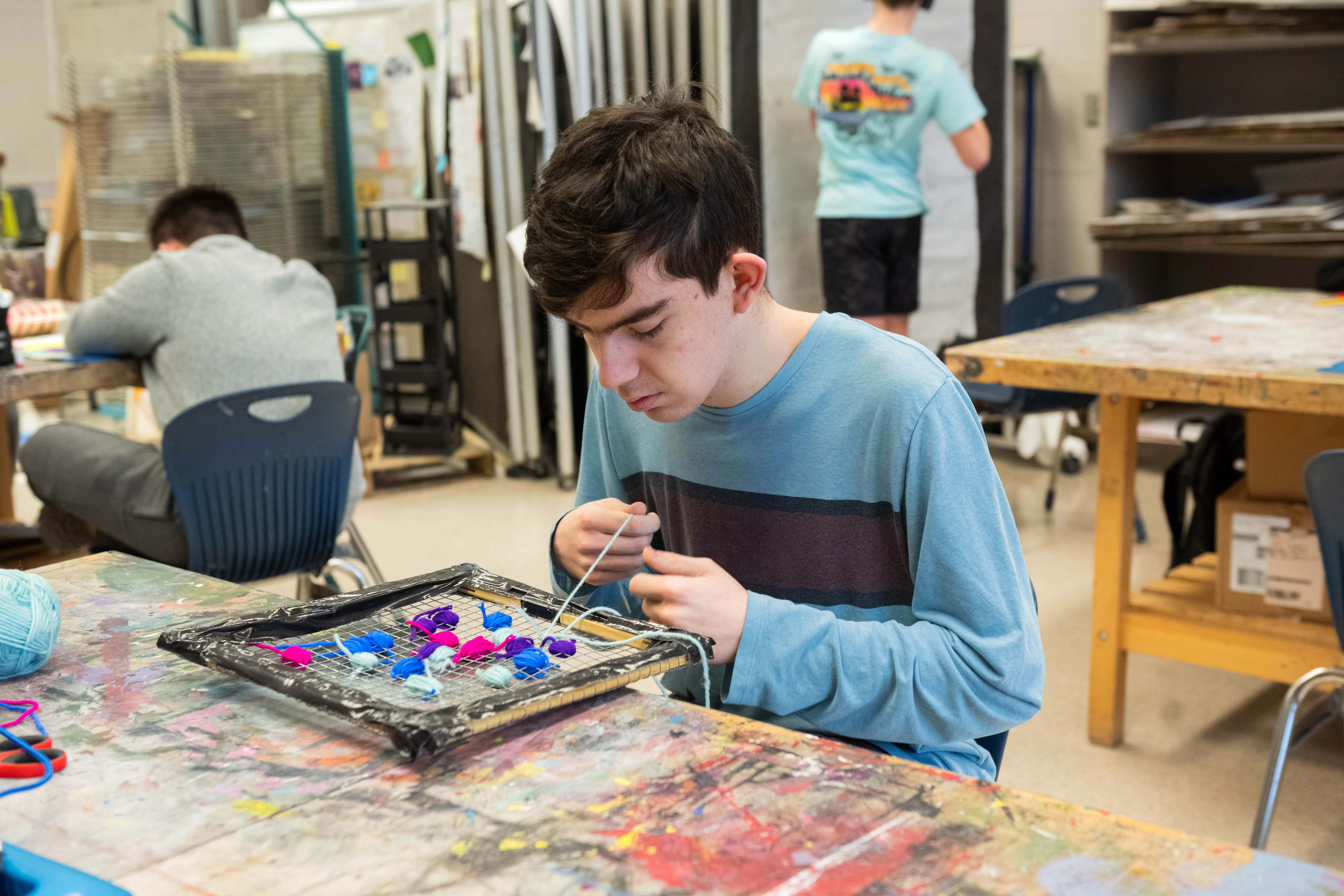 A student ties colored yarn to a wire grid. The Inclusive Fine Arts class encourages students to 