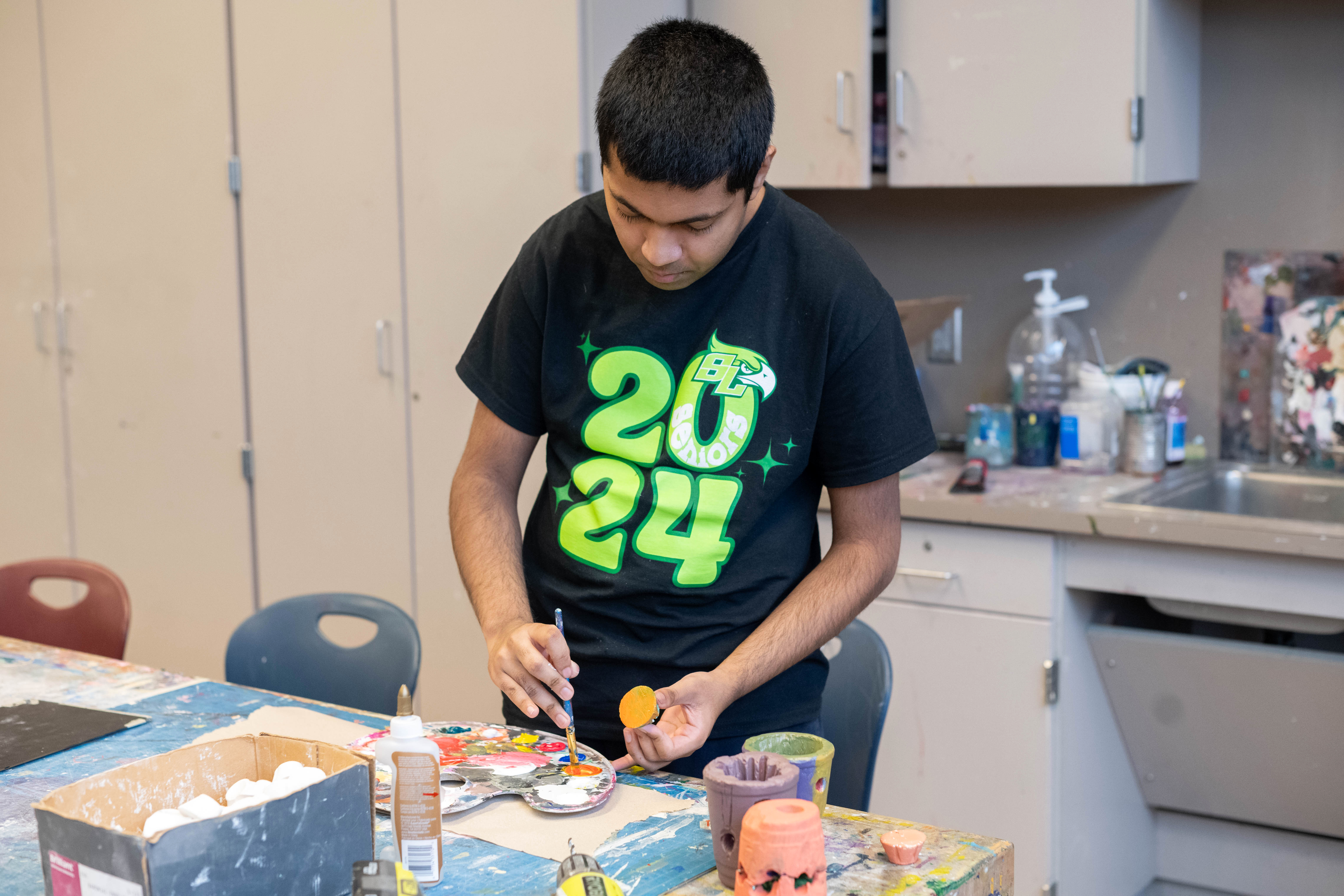 A student paints a small piece of baked clay.