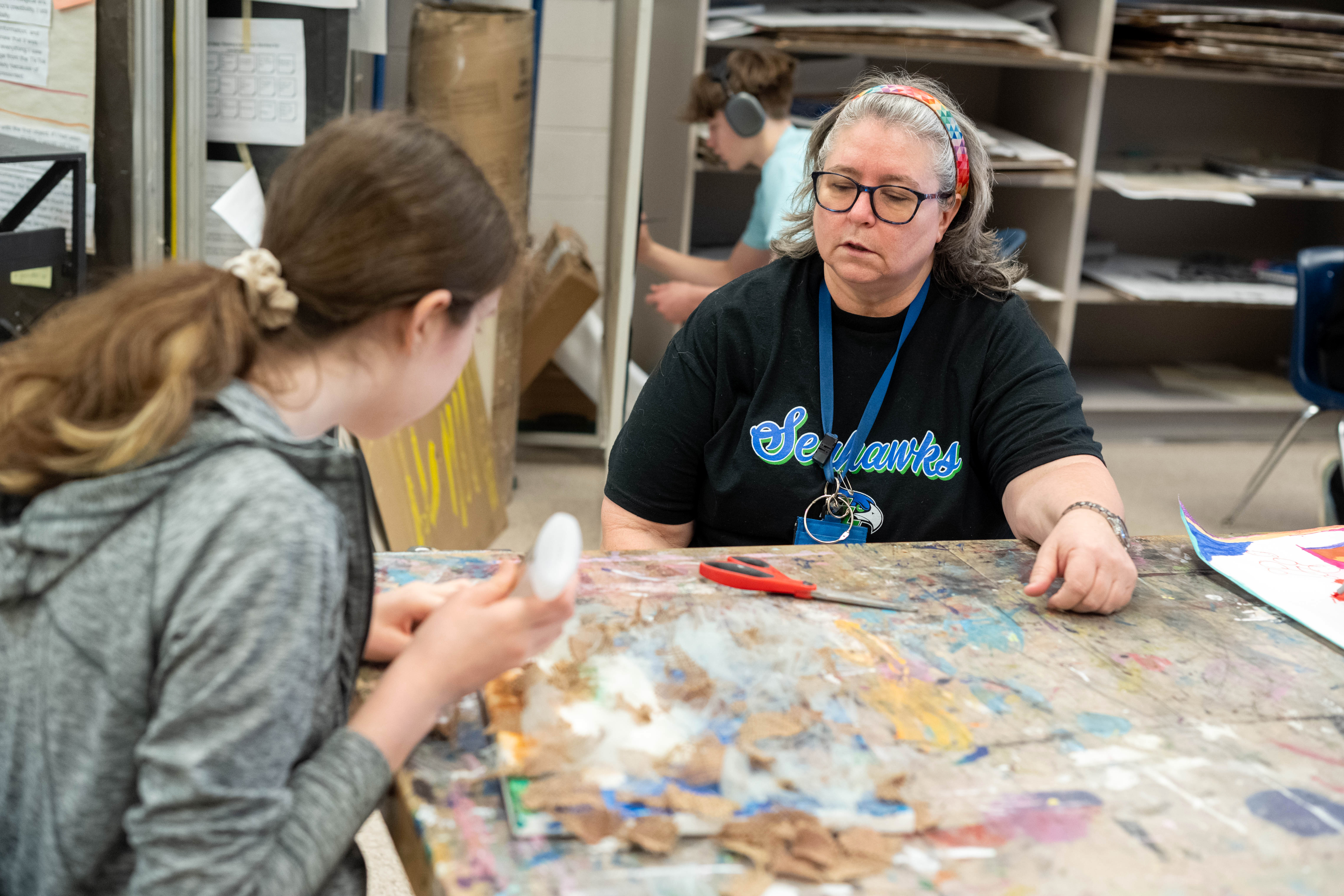 Co-teacher Claudia Harvey helps student Nora Patterson with her project - a series of fabrics glued onto canvas.
